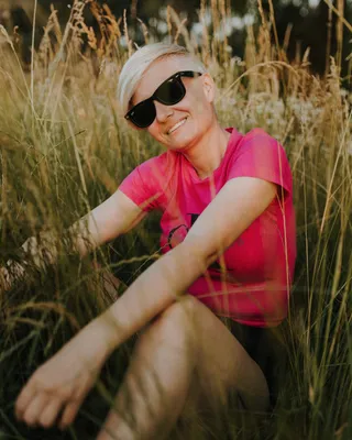 Бесплатное изображение: Молодая женщина в солнцезащитных очках сидит в  высокой траве и улыбается