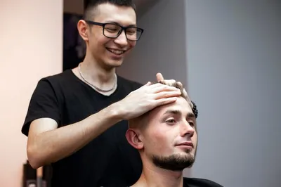 Молодой казахский парикмахер работает в парикмахерской, красивый парень  делает прическу для клиента | Премиум Фото